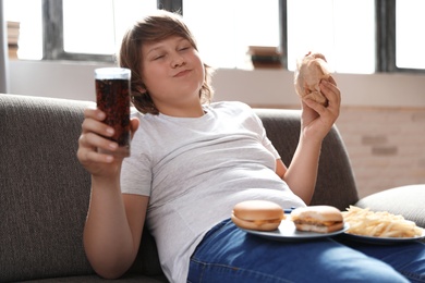 Emotional overweight boy with fast food on sofa at home