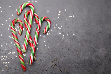 Photo of Many sweet Christmas candy canes and shiny confetti on grey background, flat lay. Space for text