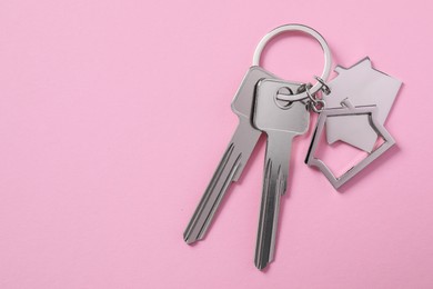 Photo of Metallic keys with keychains in shape of houses on pink background, top view. Space for text