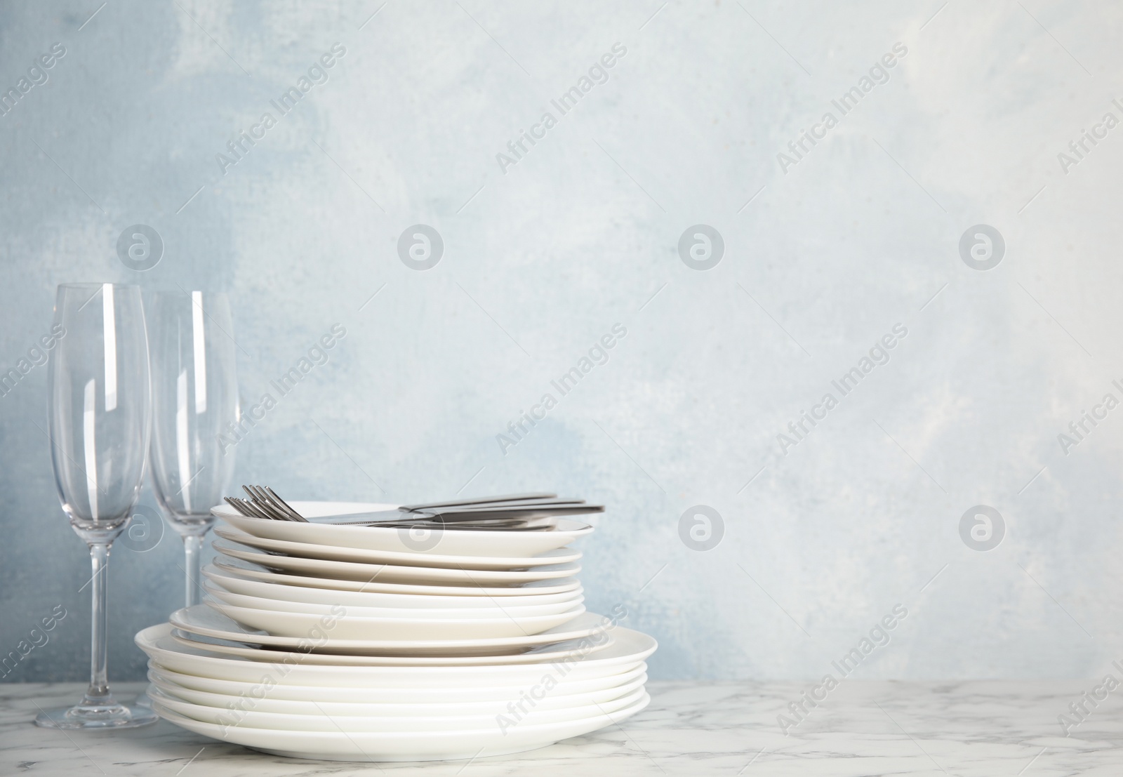 Photo of Stack of clean plates, cutlery and glasses on white marble table against light blue background. Space for text