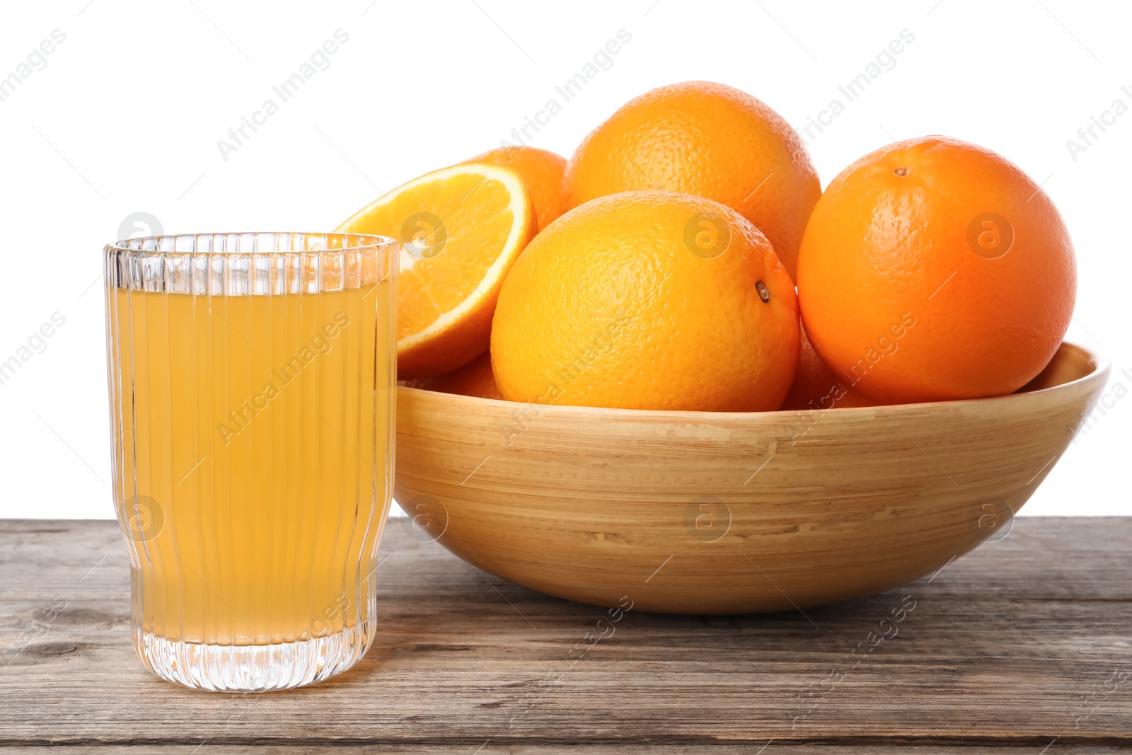 Photo of Fresh oranges in bowl and glass of juice on wooden table against white background