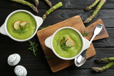 Photo of Delicious asparagus soup served on black wooden table, flat lay