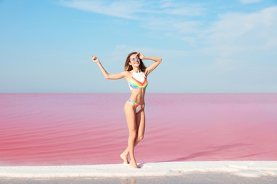 Photo of Beautiful woman in swimsuit standing near pink lake on sunny day