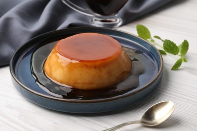 Plate of delicious caramel pudding served on white wooden table