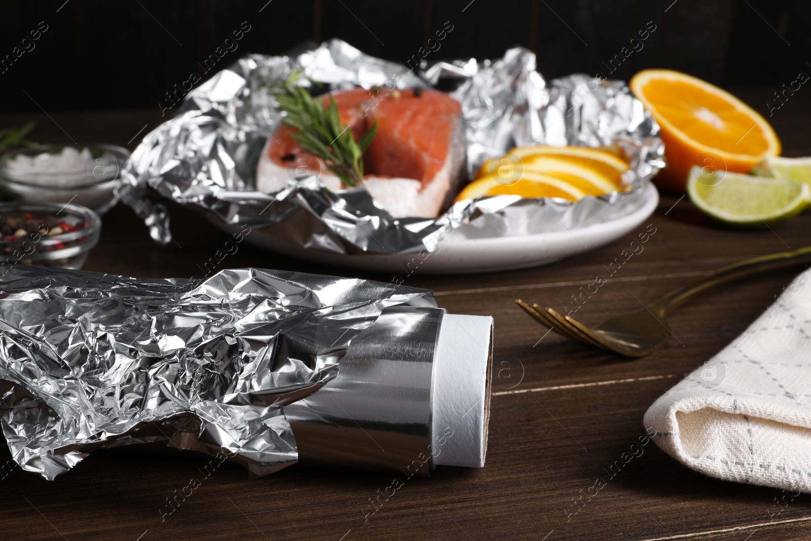 Photo of Aluminum foil, plate with salmon, rosemary and orange on wooden table, selective focus