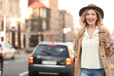 Photo of Mature woman with cup of coffee on city street