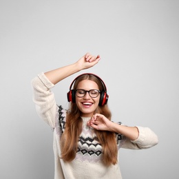 Young woman listening to music with headphones on grey background