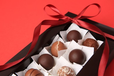 Photo of Box with delicious chocolate candies on red table, closeup