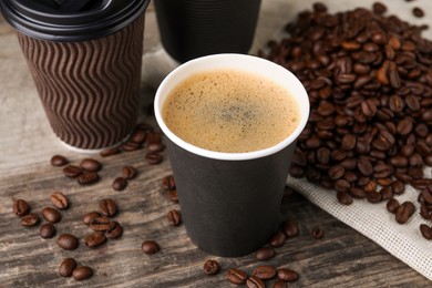 Photo of Coffee to go. Paper cups with tasty drink and roasted beans on wooden table, closeup