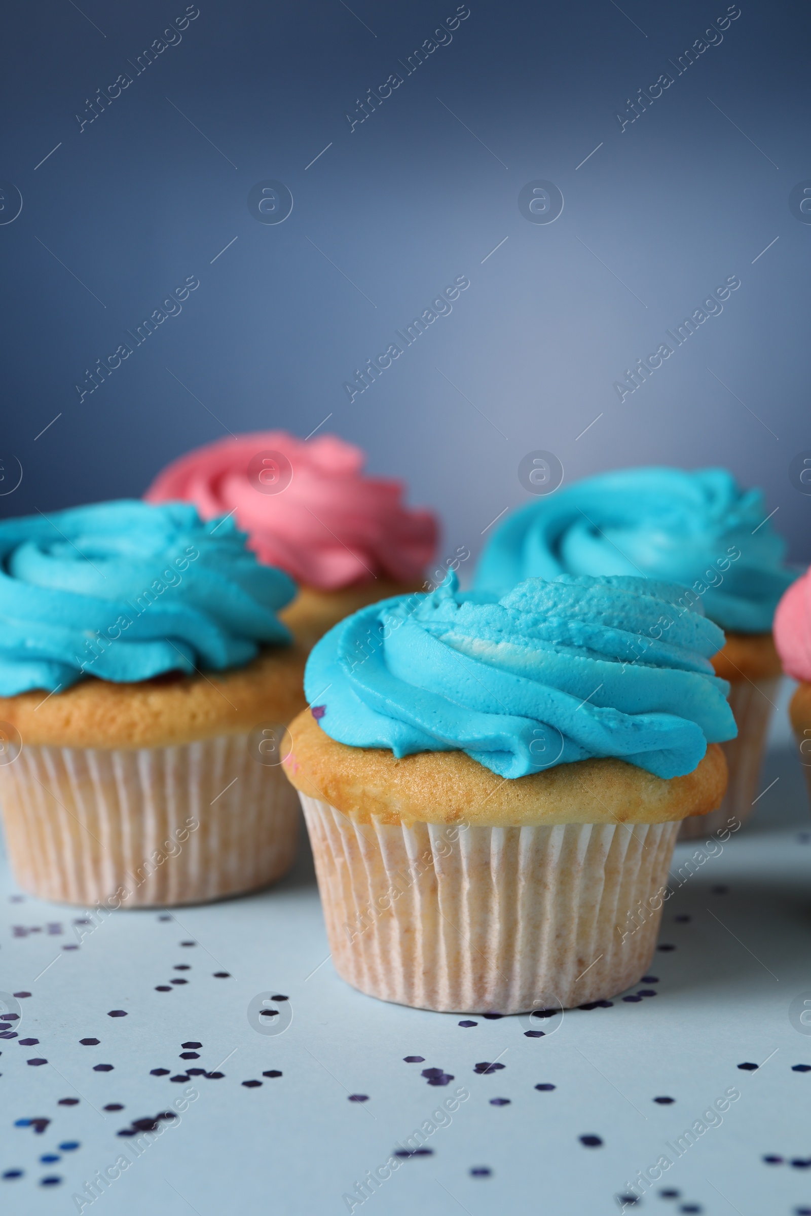 Photo of Delicious cupcakes with bright cream and confetti on blue background, closeup