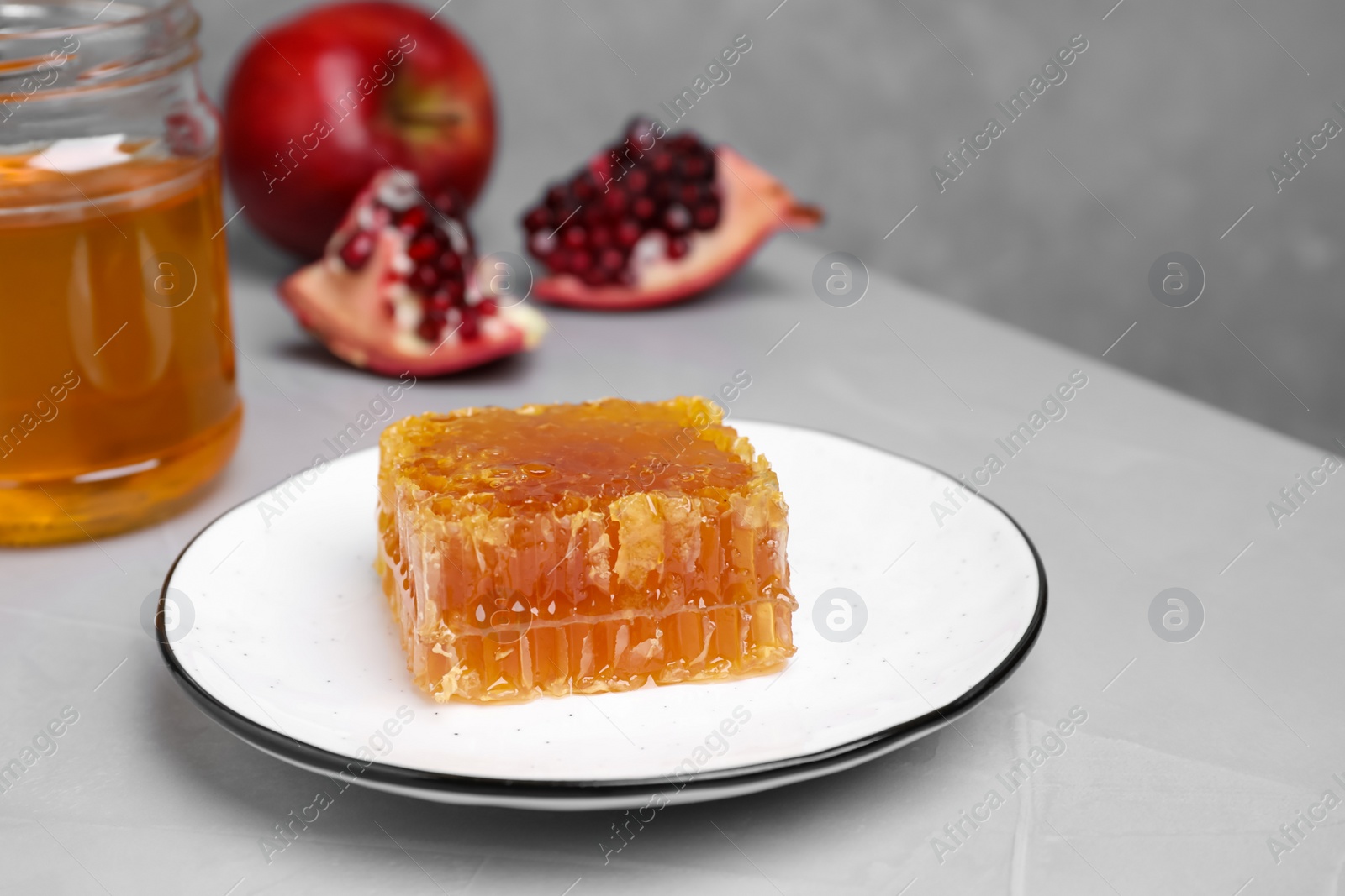 Photo of Honeycomb near pomegranate seeds and apple on light grey table. Rosh Hashanah holiday