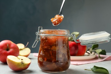 Photo of Spoon with tasty apple jam over glass jar at light table