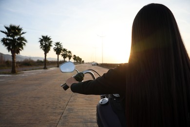 Woman riding motorcycle at sunset, back view. Space for text