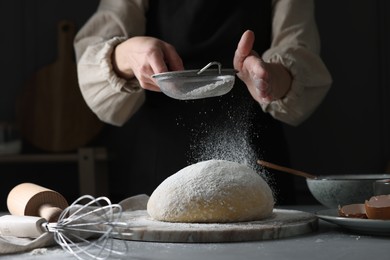 Photo of Making dough. Woman sifting flour at grey table, closeup