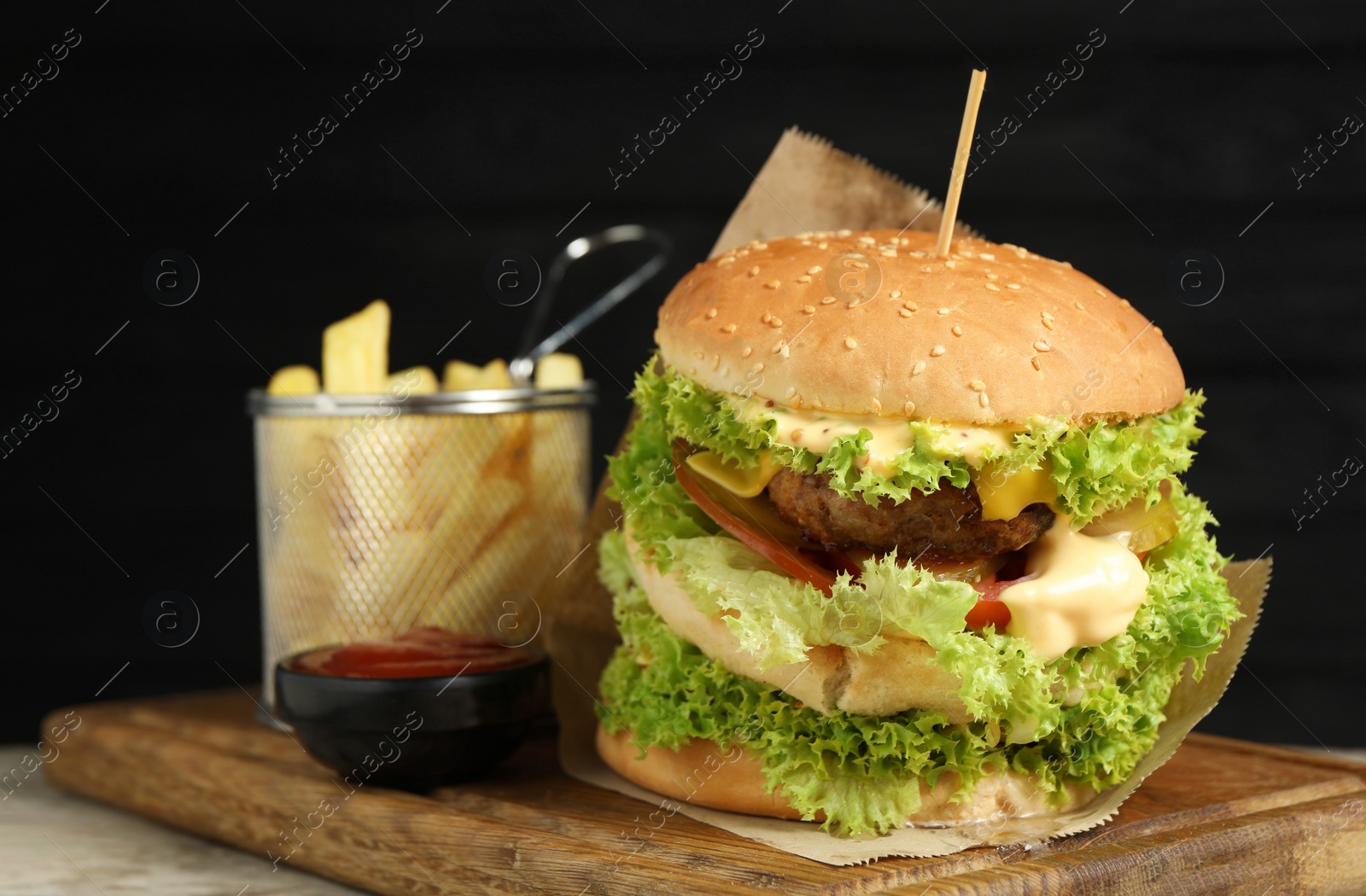 Burger with delicious patty, french fries and sauce on wooden table against dark background Photo of Burger with delicious patty, french fries and sauce on wooden table against dark background