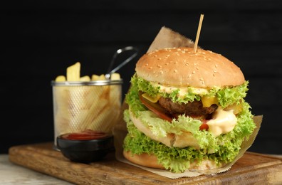 Photo of Burger with delicious patty, french fries and sauce on wooden table against dark background