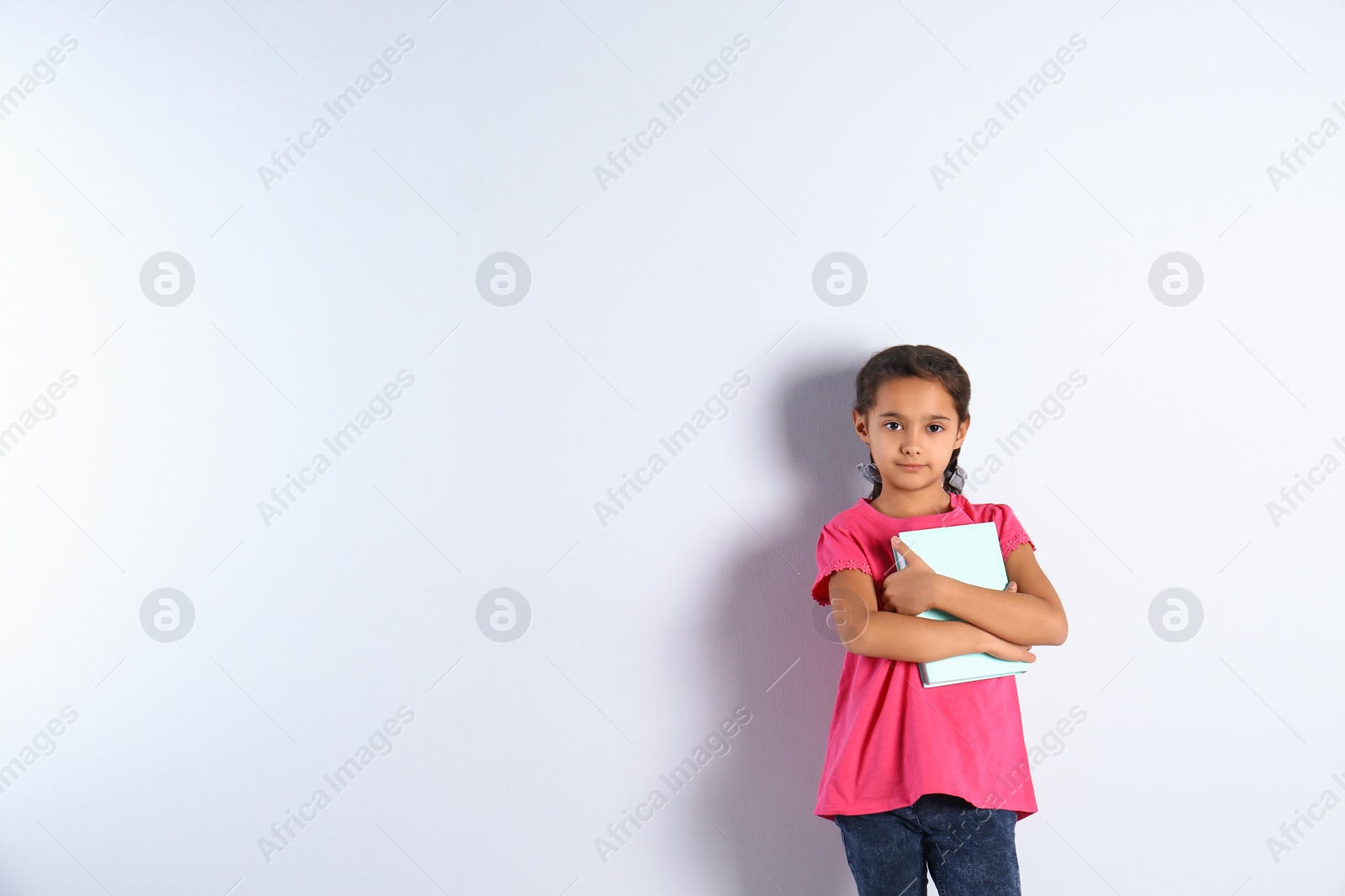 Photo of Cute little girl with book on light background,  space for text