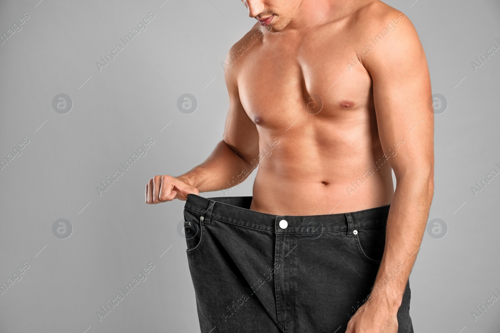 Photo of Young man with slim body in old big size jeans on grey background, closeup view. Space for text