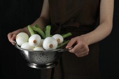 Photo of Woman holding colander with green spring onions on black background, closeup
