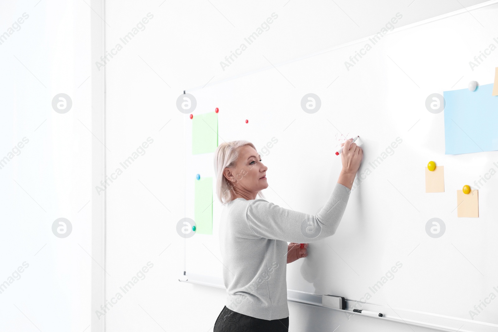 Photo of Mature teacher writing on whiteboard in classroom