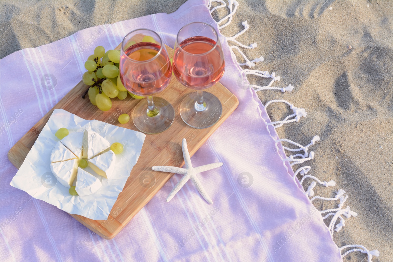 Photo of Glasses with rose wine and snacks for beach picnic on sand outdoors