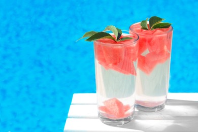 Photo of Refreshing watermelon drink in glasses near swimming pool outdoors. Space for text