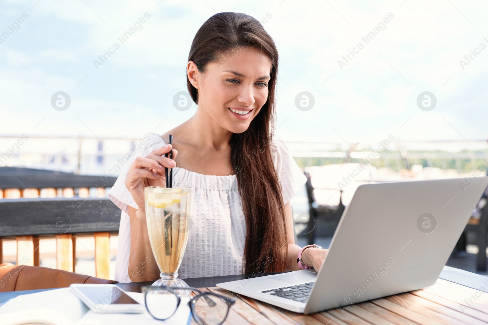 Photo of Beautiful woman with laptop and refreshing drink at outdoor cafe