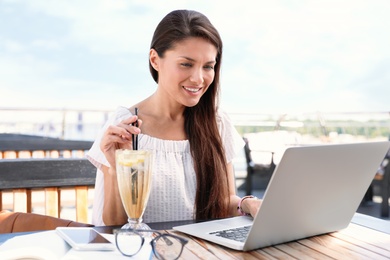 Beautiful woman with laptop and refreshing drink at outdoor cafe