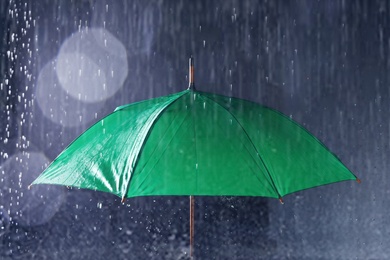 Photo of Bright umbrella under rain on dark background