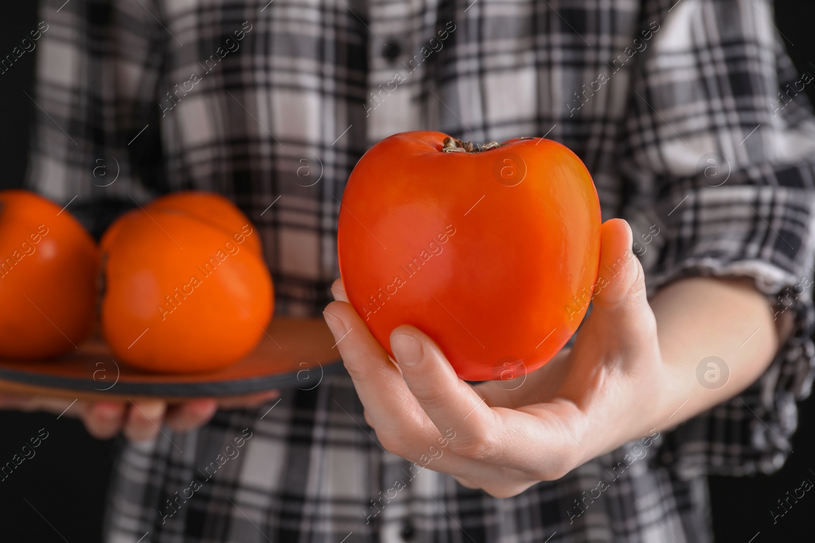 Photo of Woman holding delicious ripe juicy persimmons on black background, closeup