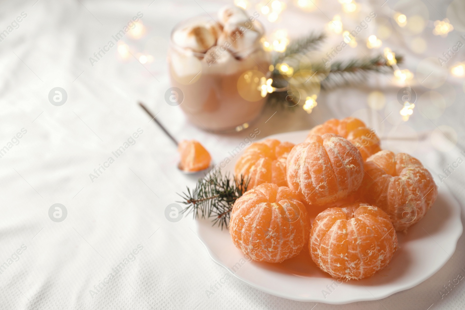 Photo of Peeled delicious ripe tangerines and glass of drink with marshmallows on white bedsheet. Space for text