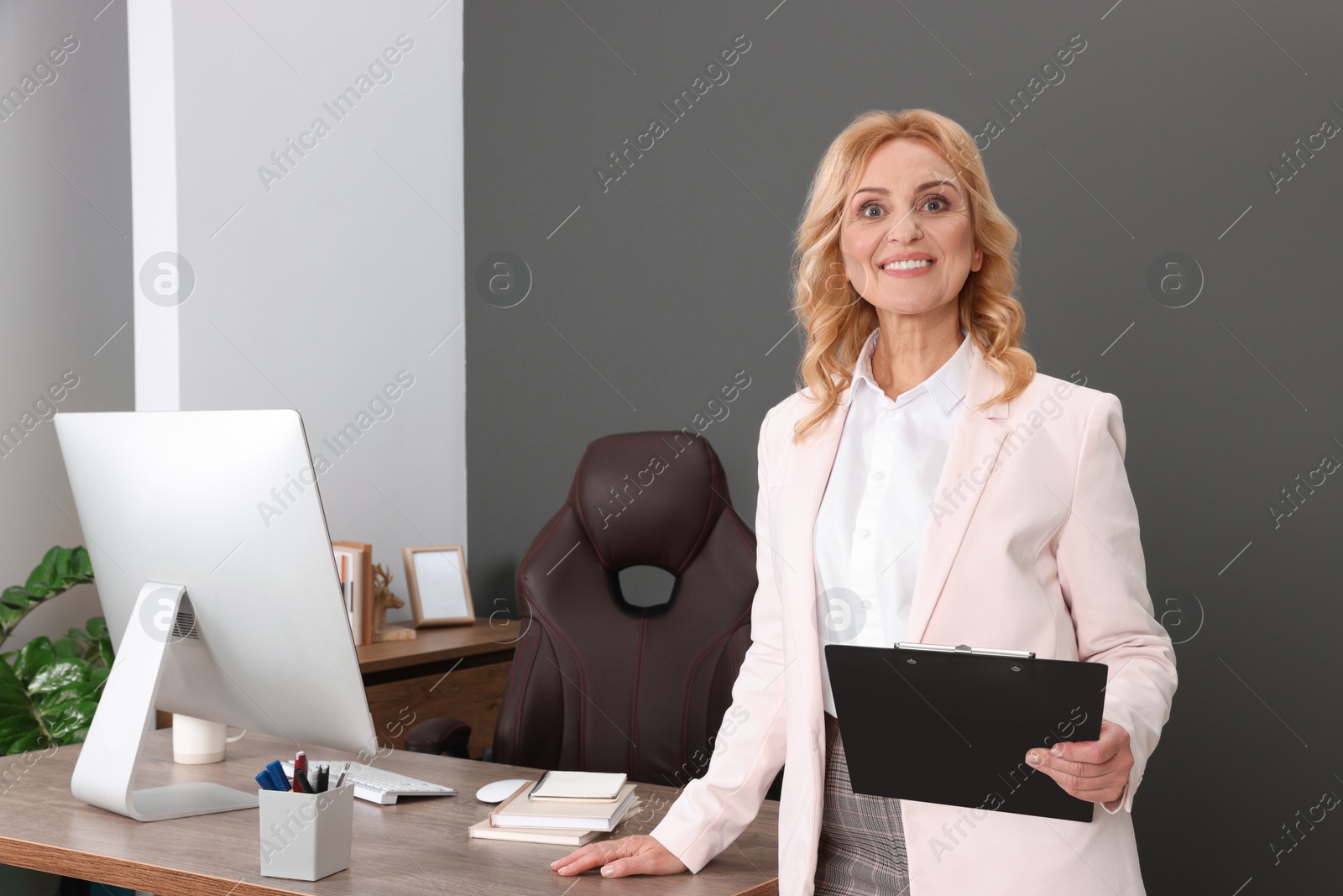 Photo of Happy lady boss with clipboard near desk in office. Successful businesswoman