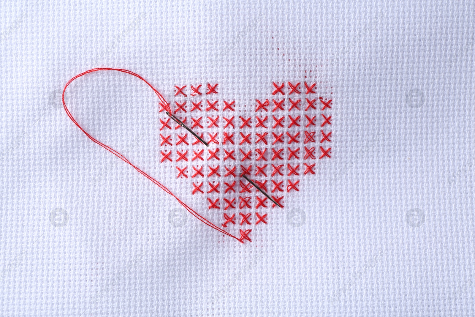 Photo of Embroidered red heart and needle on white cloth, top view