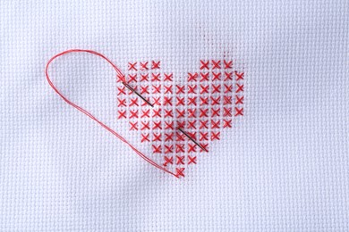 Embroidered red heart and needle on white cloth, top view