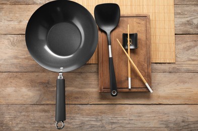 Black metal wok, chopsticks and spatula on wooden table, top view