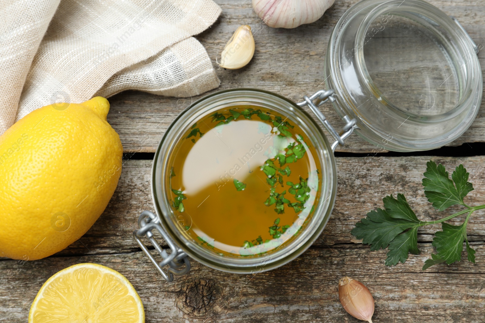 Photo of Jar with lemon sauce and ingredients on wooden table, flat lay. Delicious salad dressing