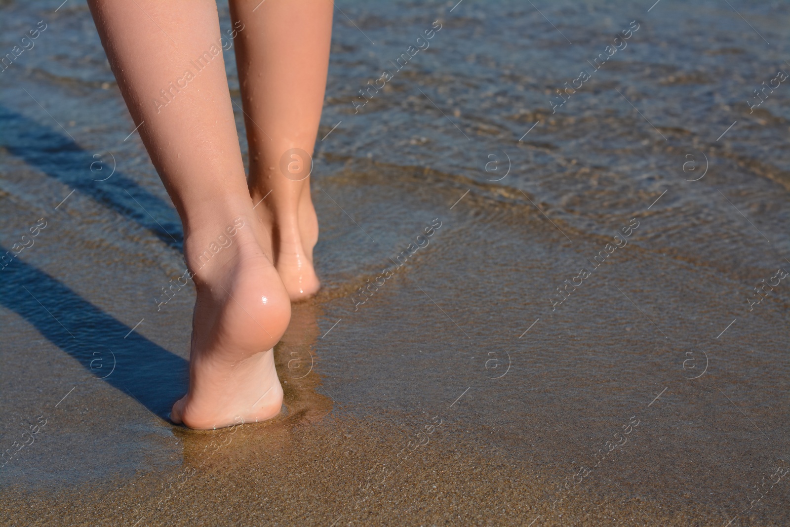 Photo of Child walking through water on seashore, closeup of legs. Space for text