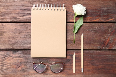 Photo of Notebook, eustoma flower, sunglasses and pencils on wooden background, flat lay