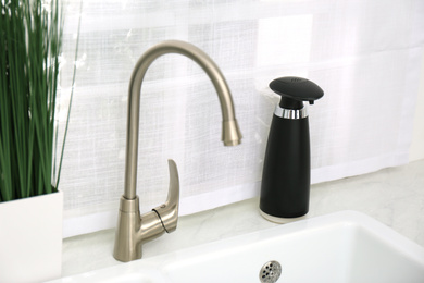 Photo of Modern automatic soap dispenser near sink in kitchen