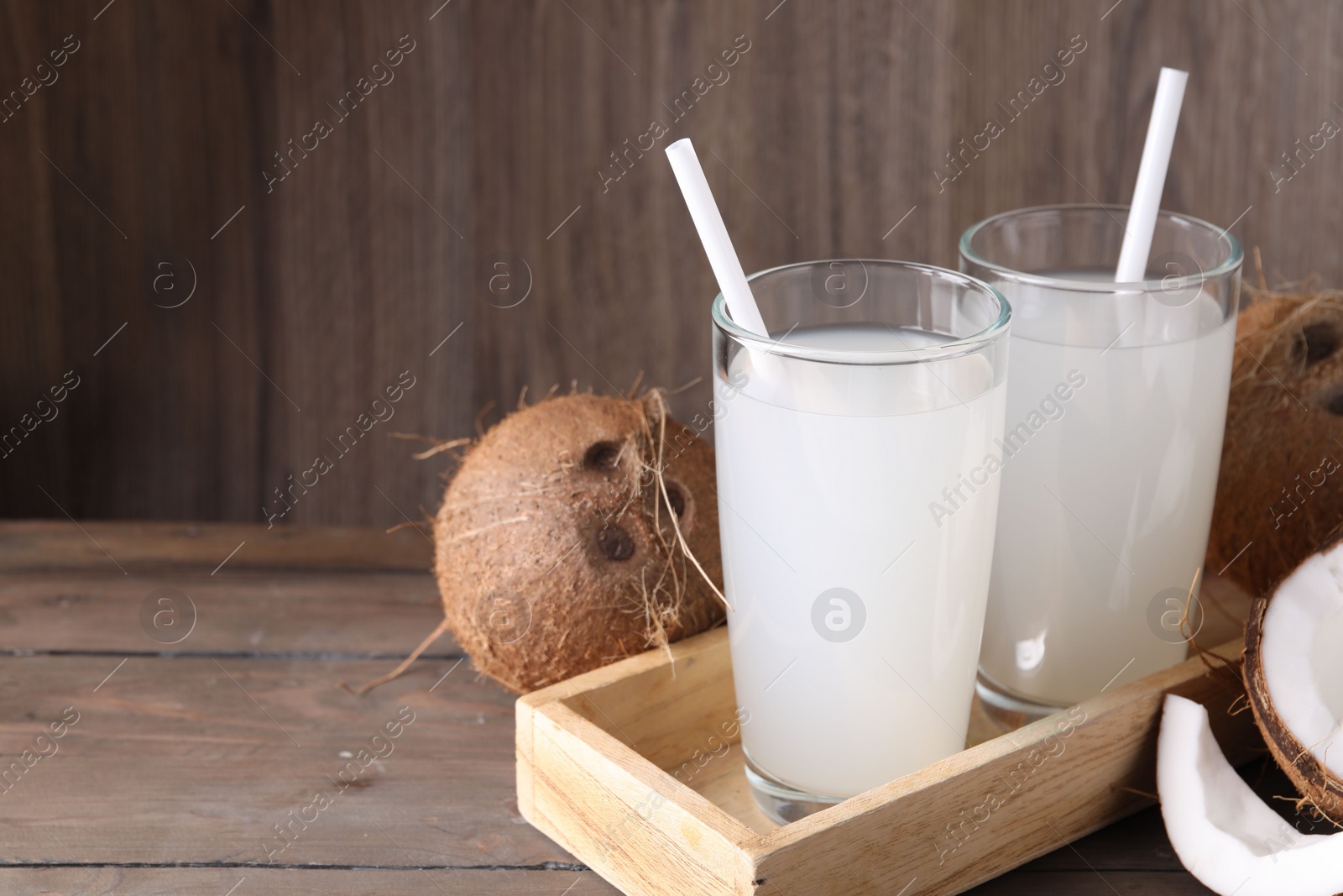 Photo of Glasses of coconut water with straws and nuts on wooden table, space for text