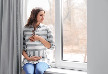 Beautiful pregnant woman near window at home