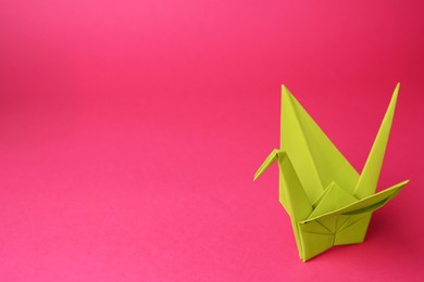 Photo of Origami art. Handmade paper crane on pink background, space for text