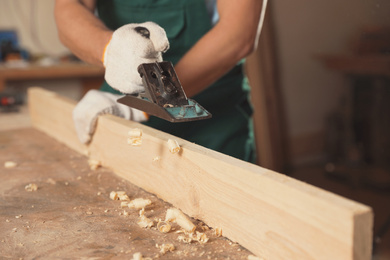 Professional carpenter grinding wooden plank with jack plane in workshop, closeup