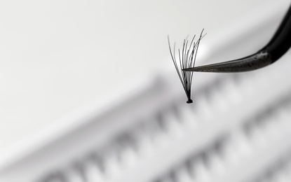 Woman holding tweezers with false eyelash, closeup