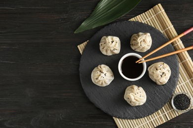 Slate plate with tasty baozi dumplings, chopsticks and soy sauce served on wooden table, top view. Space for text