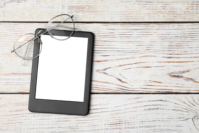 Photo of Modern e-book reader and glasses on wooden table, top view. Space for text