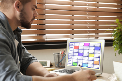 Photo of Young man using calendar app on laptop in office, closeup