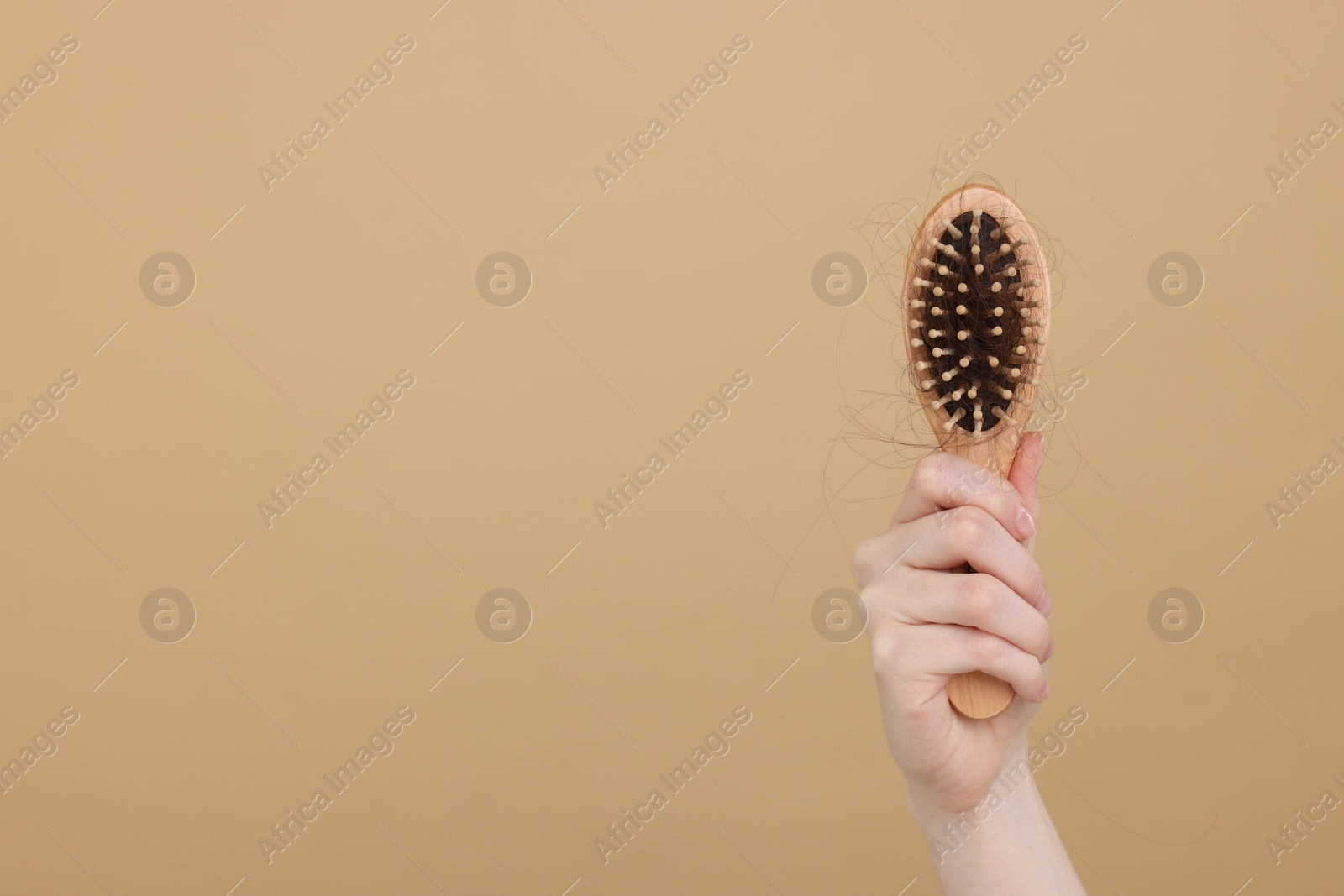 Photo of Woman holding brush with lost hair on beige background, closeup and space for text. Alopecia problem