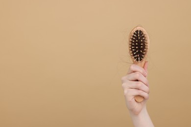 Photo of Woman holding brush with lost hair on beige background, closeup and space for text. Alopecia problem