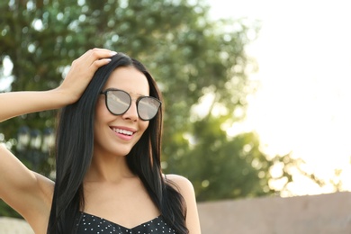 Beautiful young woman wearing stylish sunglasses outdoors. Space for text